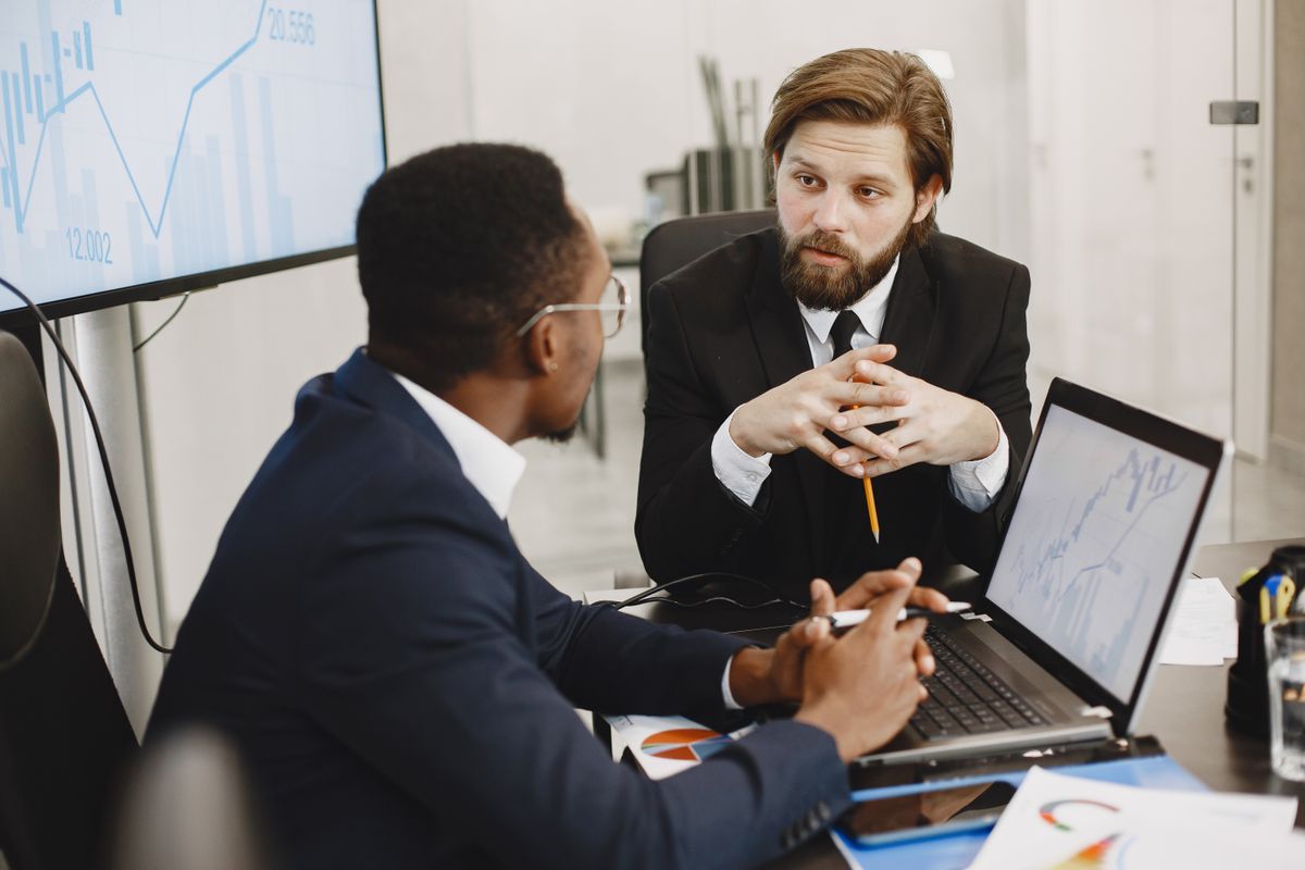 Two professionals in suits reviewing financial charts on a laptop in a modern office